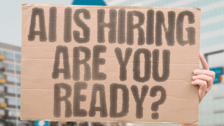 Person holding up a sign saying "AI is hiring - are you ready?"