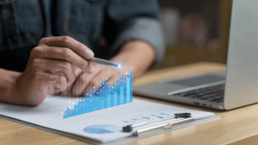 Picture visualising Tech Trends 2025: Person holding pen, pointing at digital graph